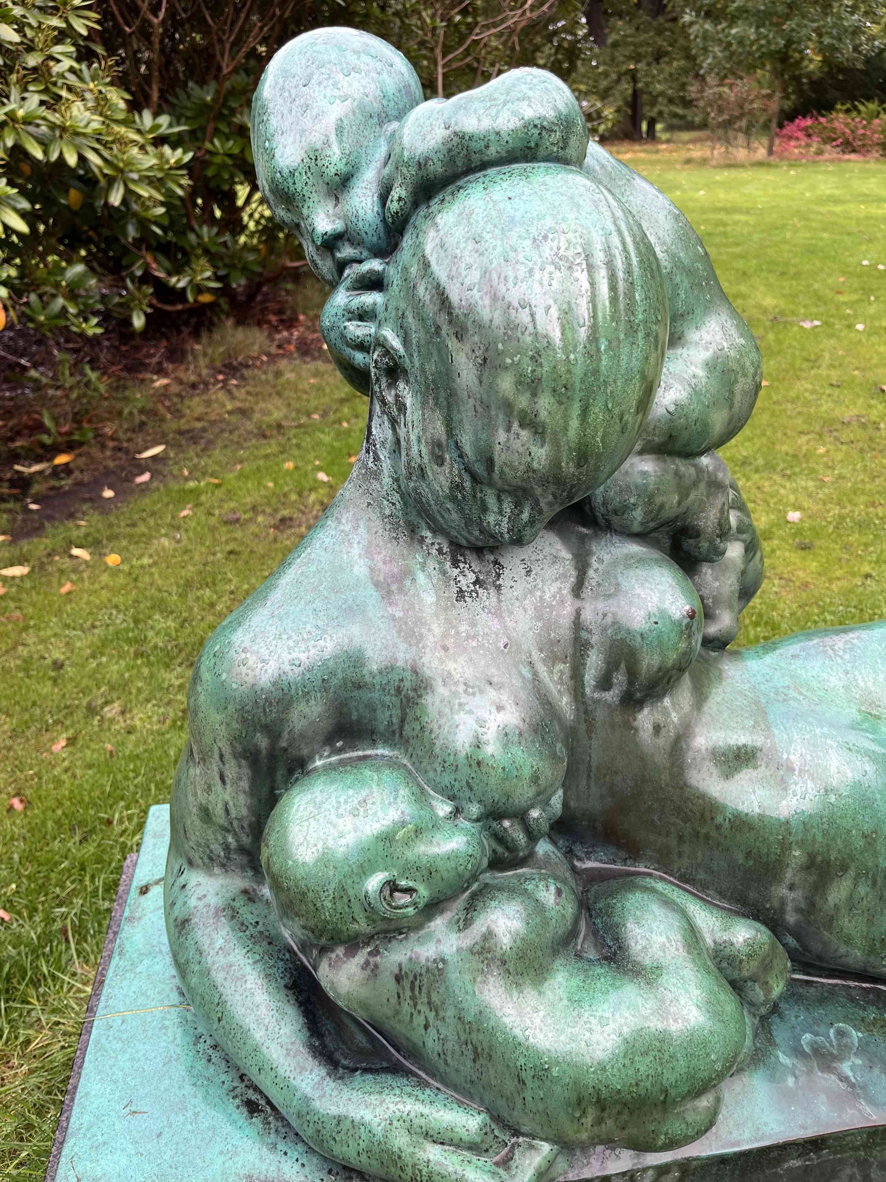 Bronzeskulptur af en kvinde med børn i en grøn have